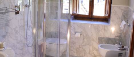 A modern bathroom with a glass-enclosed shower, a marble-tiled floor, a sink, and a bidet.