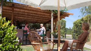 An outdoor patio with wicker chairs, a table, and a white umbrella providing shade. - Hotel Villa Cappugi (Pistoia)