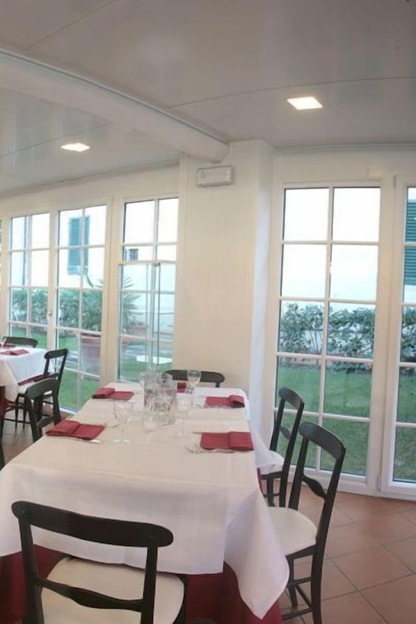 A dining area with tables set for two, large windows, and a view of the outdoors. - Hotel Villa Cappugi (Pistoia)