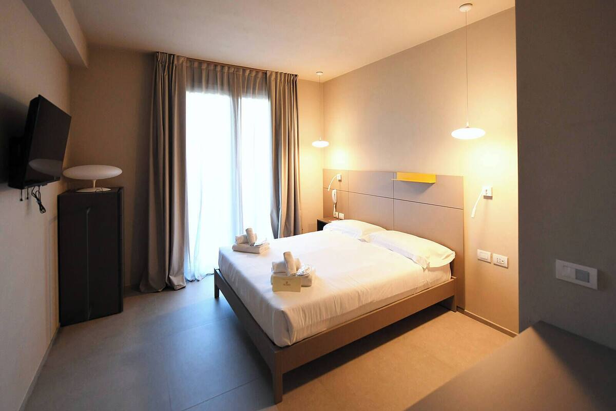 A hotel room with a bed, bedside lamps, a flat-screen TV, and a window with curtains.