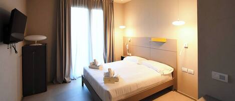 Habitación de hotel con cama, lámparas de noche, televisión de pantalla plana y ventana con cortinas.
