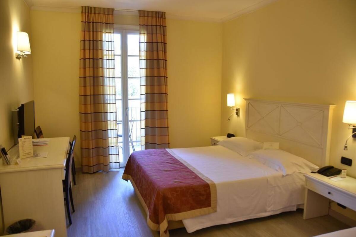 A hotel room with a bed, bedside tables, a desk, and a chair.
