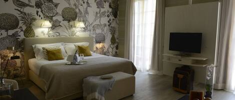 A hotel room with a large bed, bedside lamps, a TV, and a desk with a vase of flowers.