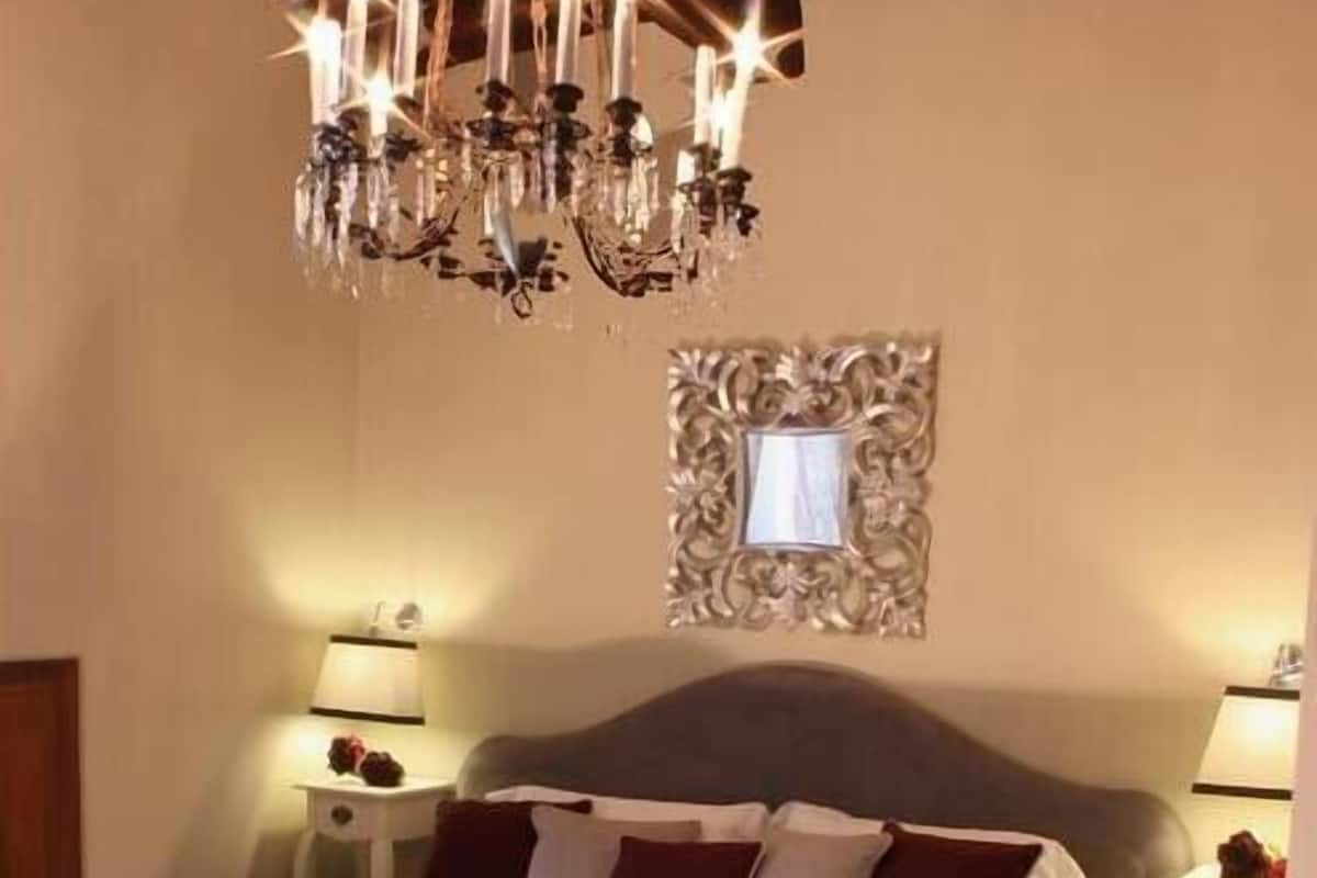 A bedroom with a large bed, a chandelier, two bedside tables with lamps, and a decorative mirror on the wall.