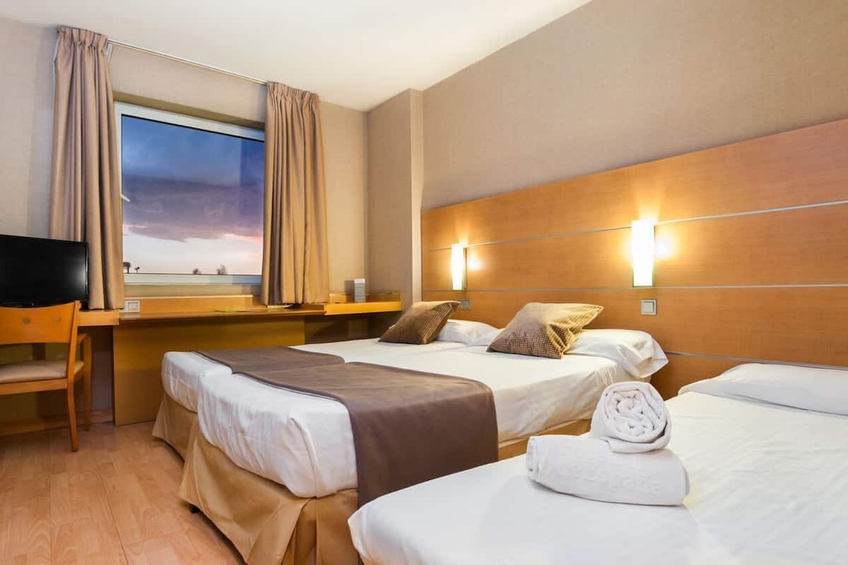 Une chambre d’hôtel avec deux lits, un bureau, une chaise, une télévision et une fenêtre avec des rideaux.