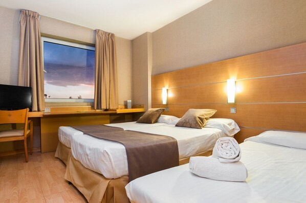 Una habitación de hotel con dos camas, un escritorio, una silla, un televisor y una ventana con cortinas.
