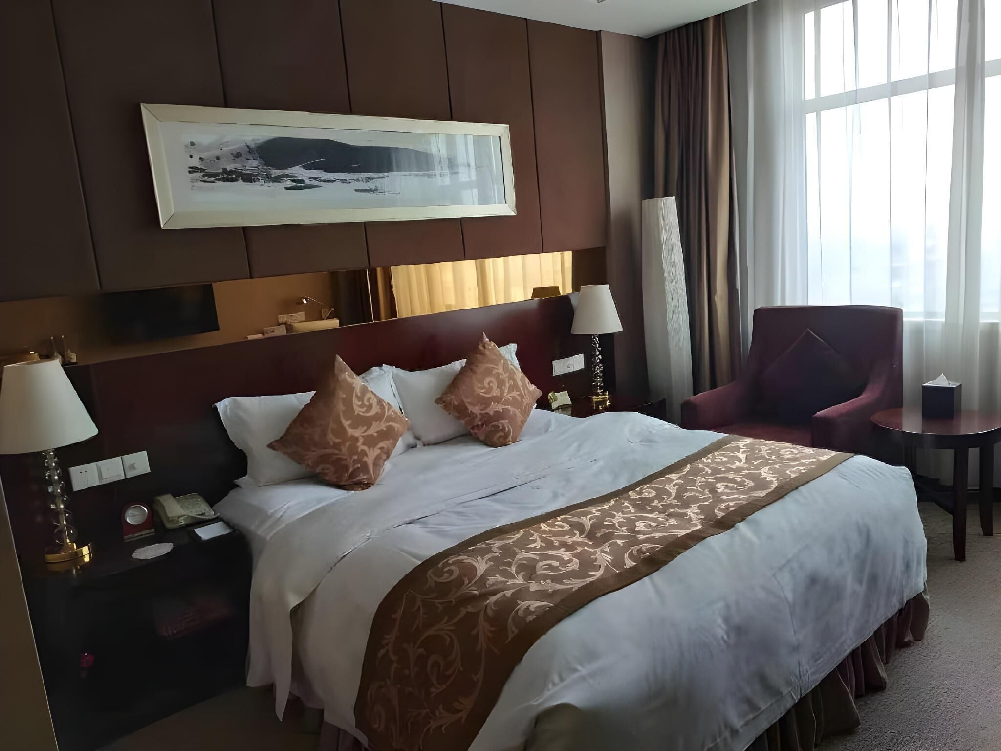 Habitación de hotel con una cama grande, dos mesitas de noche, una silla, un escritorio y una ventana con cortinas.