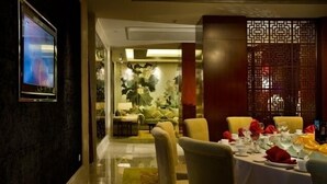 A hotel dining area with a table set for a meal, a television mounted on the wall, and a decorative partition with intricate patterns. - Grand Soluxe International HOT (Xi'an)