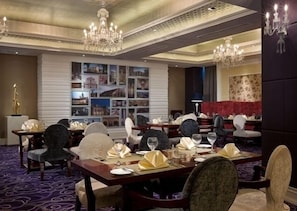 A dining area with multiple tables set for service, a chandelier, and a wall with framed pictures.