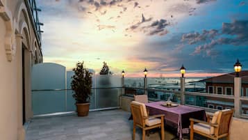 Una terraza con mesa y sillas, con vistas a un paisaje urbano al atardecer.