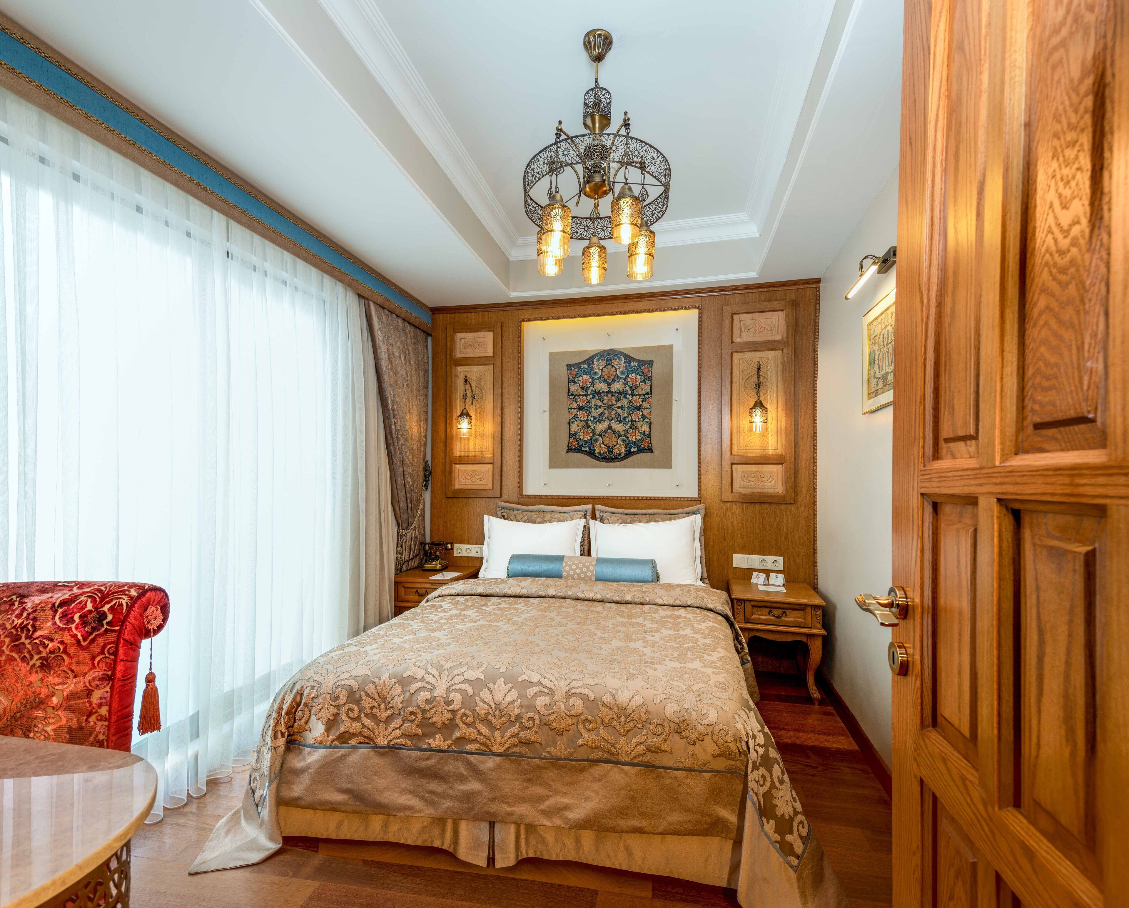 A hotel room with a large bed, wooden paneling, a chandelier, and a red armchair.