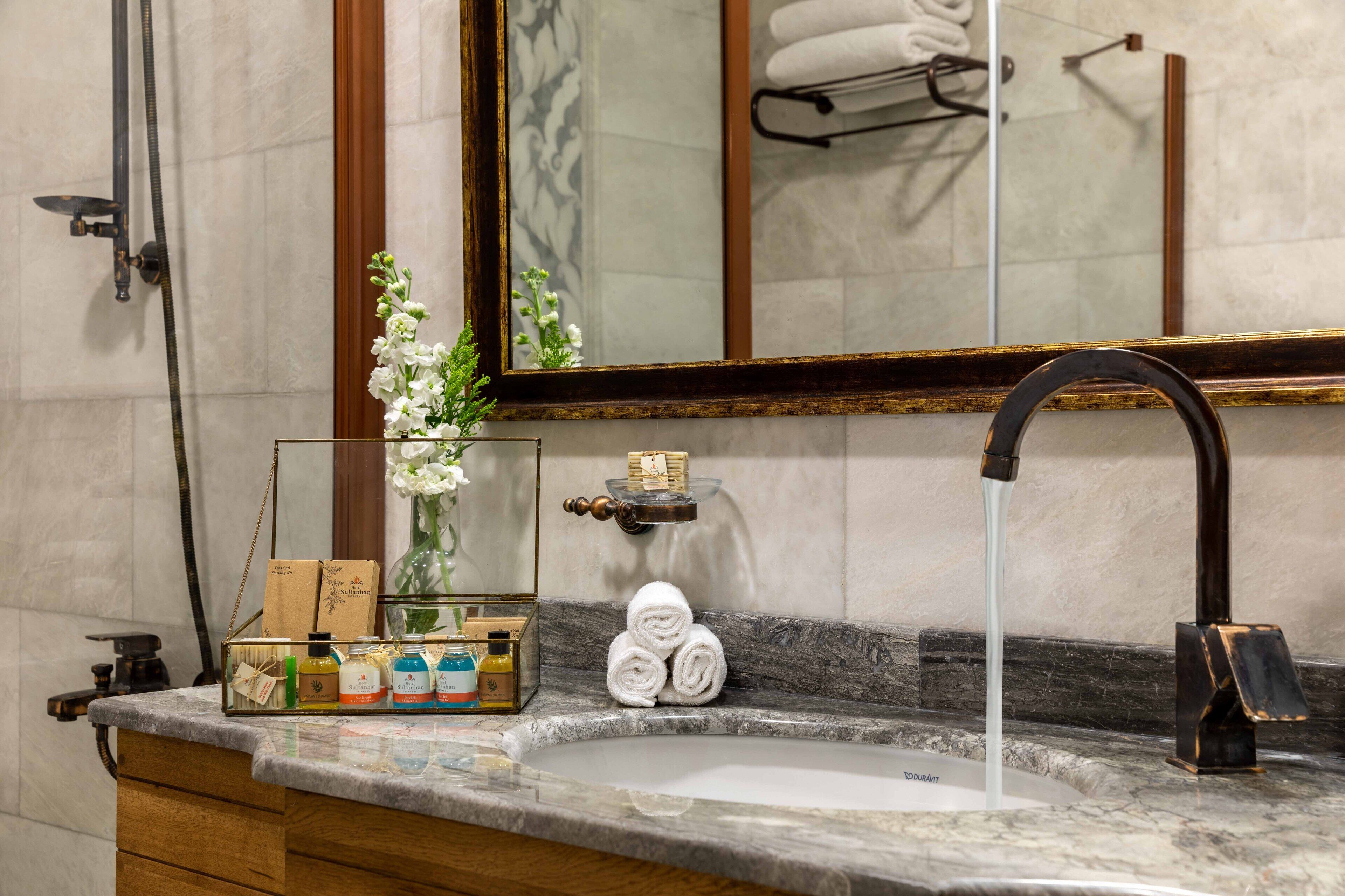 A bathroom with a marble sink, a large mirror, a towel rack, and a shower with a handheld showerhead.