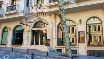 Un edificio storico con un'ampia entrata ad arco, un albero di fronte e una strada acciottolata.