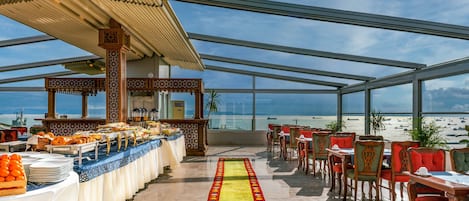 Restaurante en la azotea con servicio de buffet, mesas y sillas para comer, con vistas a la playa.