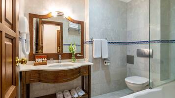 Un baño con tocador de madera, un espejo grande, cabina de ducha de vidrio y un inodoro blanco.