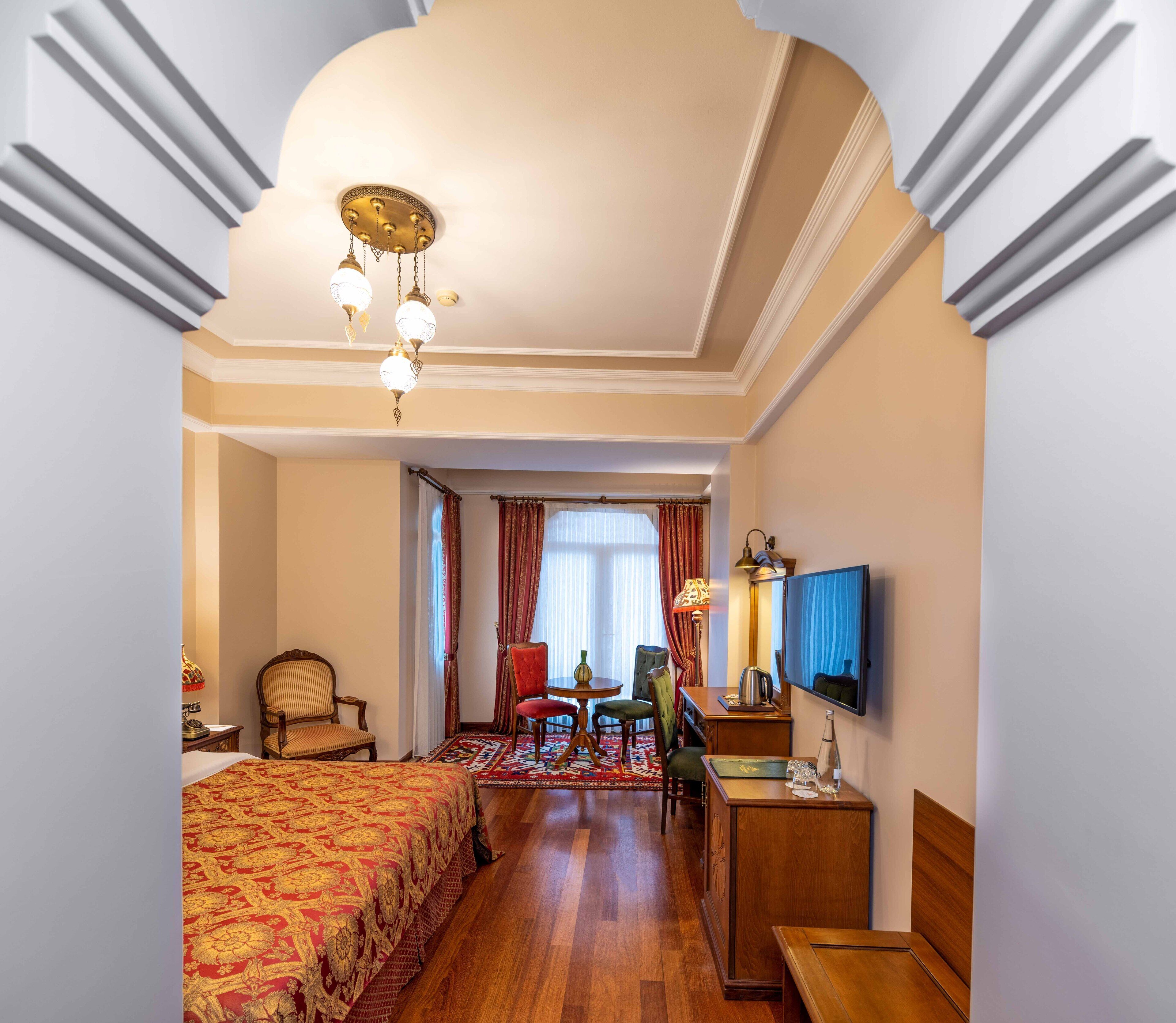 A hotel room with a large bed, a desk, a chair, a television, and a chandelier.