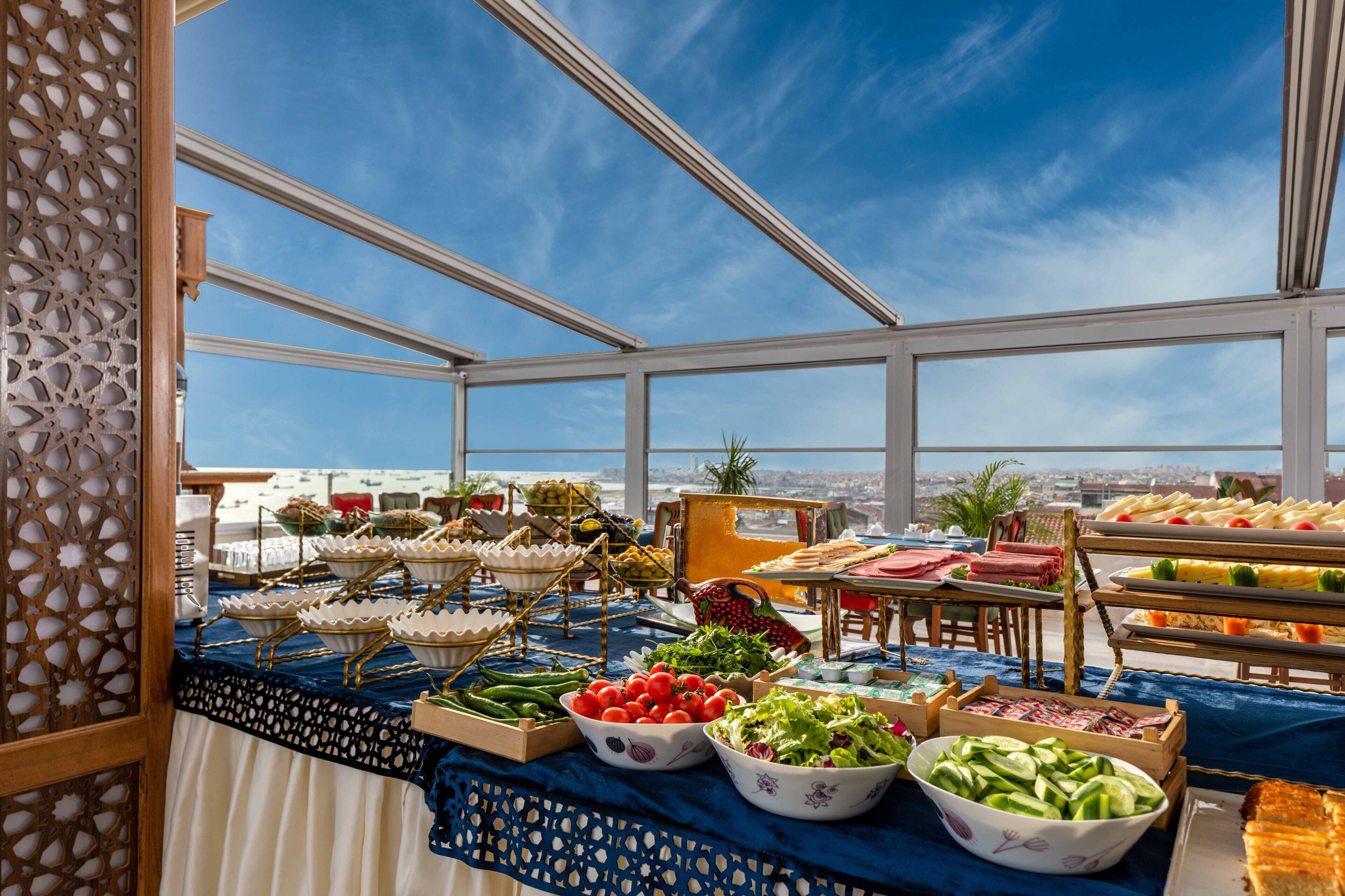 A buffet table with various food items and a view of the city through large windows.