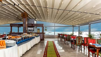 A spacious dining area with a long table, chairs, and a view of the sea.