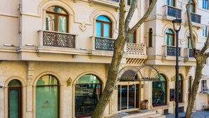 La façade d’un hôtel, ornée d’arcs en plein cintre au niveau des fenêtres, d’un balcon doté d’une rampe ouvragée et d’un lampadaire.