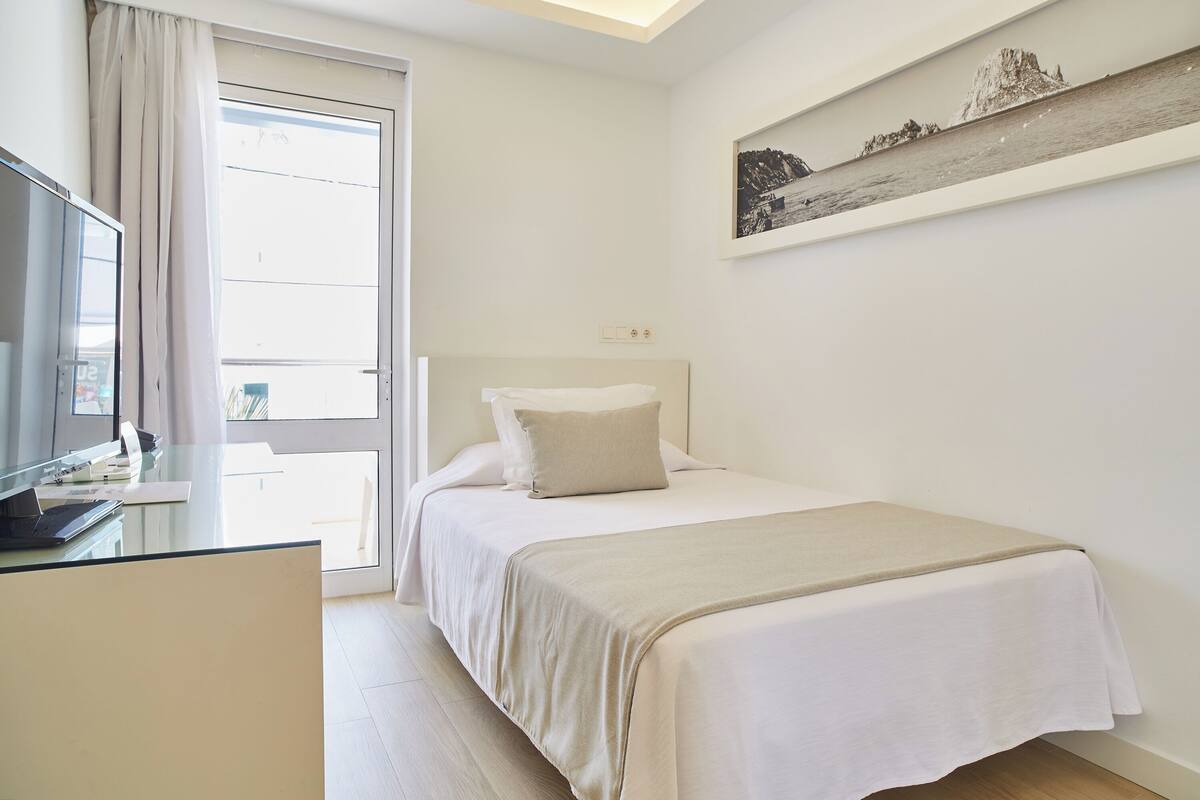 A bedroom with a bed, a desk, and a window.