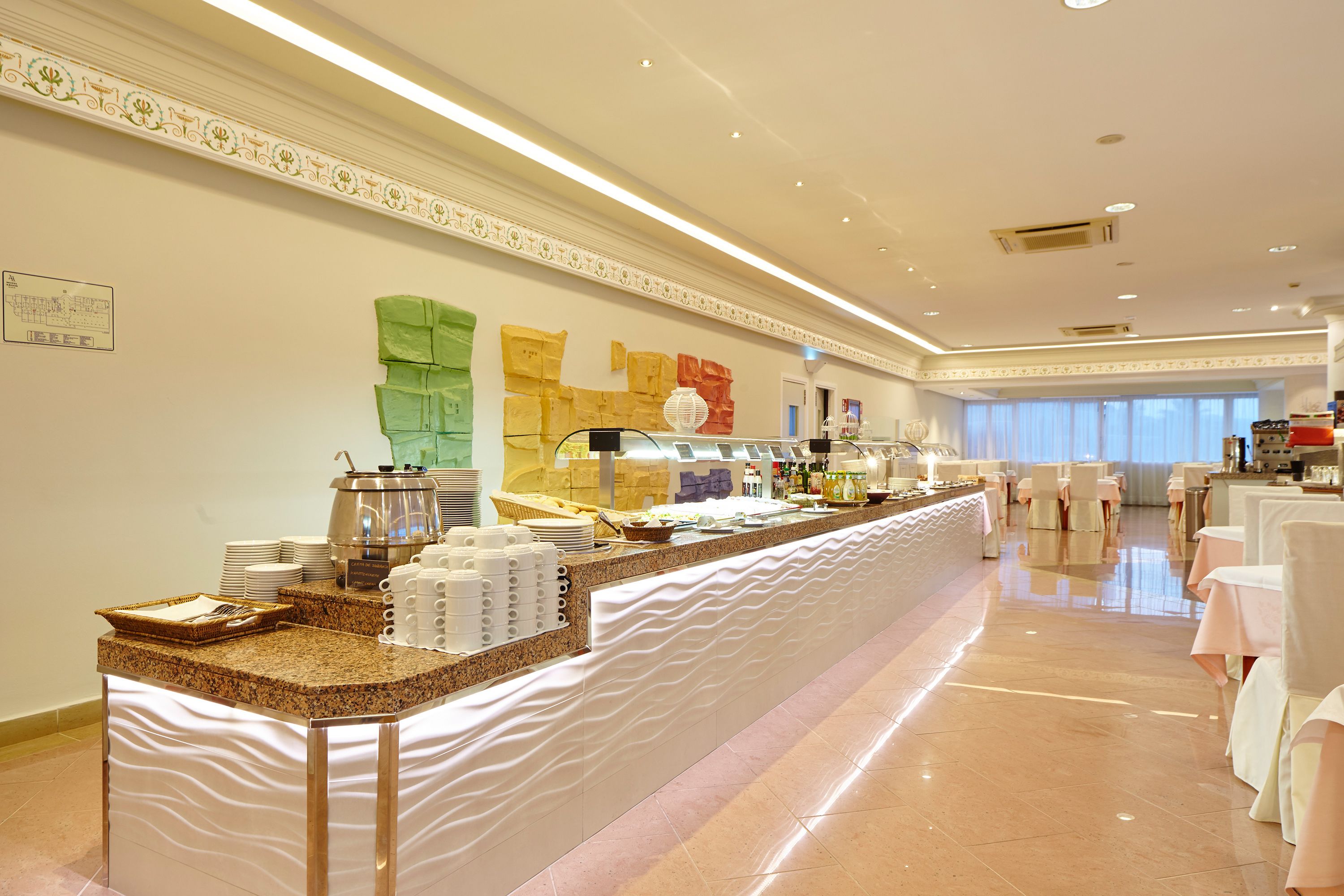 A buffet area with a long counter, various food stations, and a seating area with round tables and chairs.