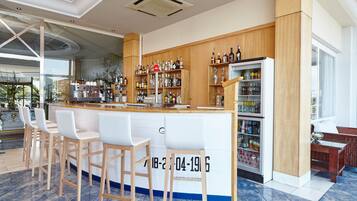 Zona de bar moderna con mostrador de madera, taburetes blancos y estantes llenos de botellas.