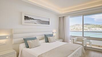 Una habitación de hotel moderna con una cama grande, una mesita de noche, una silla y vistas al mar.