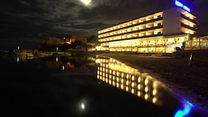A hotel with multiple floors and balconies, a reflective pool in the foreground, and a moonlit sky. - Argos Hotel (Ibiza Town)