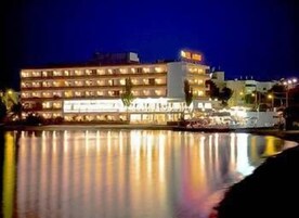 Um hotel com vários andares, janelas iluminadas e uma área de piscina em primeiro plano.