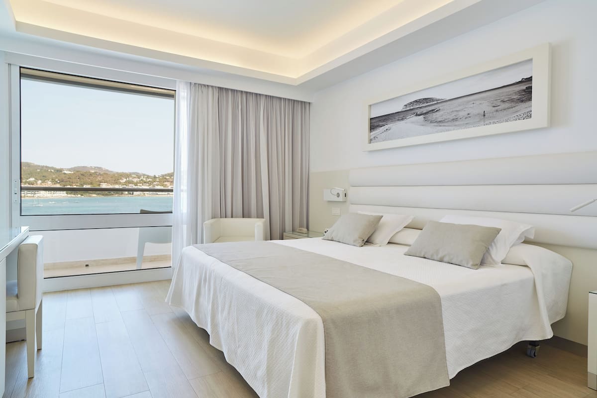 A modern hotel room with a large bed, a desk, and a view of the sea.
