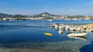 A marina with boats docked, clear water, and a hilly town in the background. - Argos Hotel (Ibiza Town)