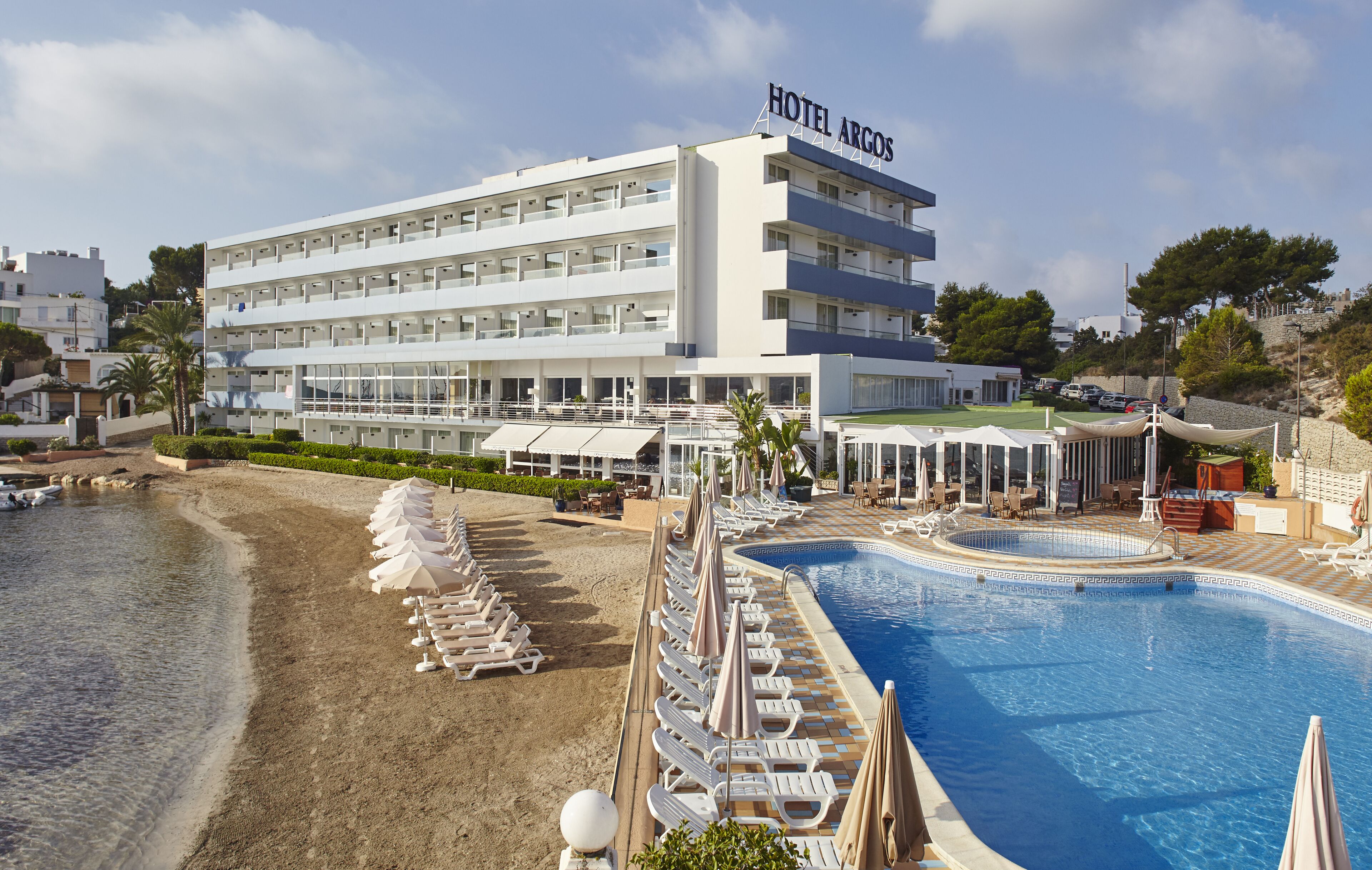 Een hotel met een zwembad, ligbedden aan het strand en uitzicht op zee.