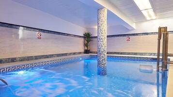 Una piscina interior con suelo y paredes de azulejos, una columna central y un cartel de prohibido fumar en la pared.