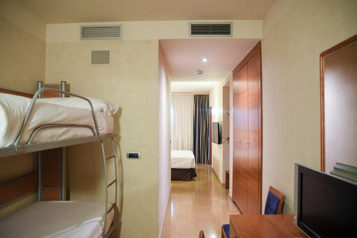 A hotel room with bunk beds, a desk, a television, and a wardrobe.