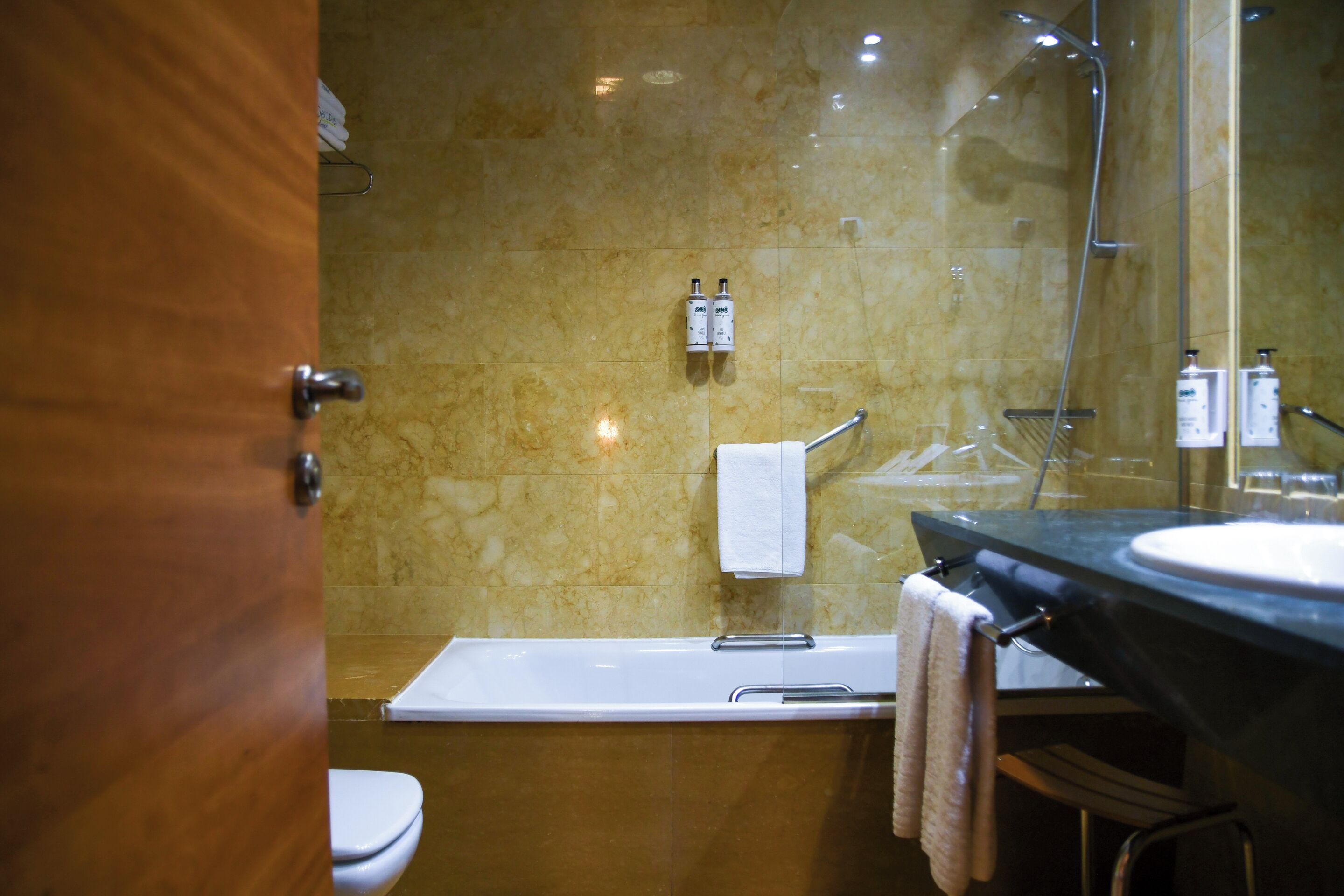 Un baño con una bañera, un lavabo y un inodoro. Hay dos botellas de champú y una toalla colgada en la pared.