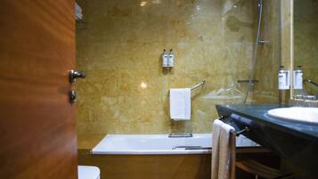 Un baño con una bañera, un lavabo y un inodoro. Hay dos botellas de champú y una toalla colgada en la pared.