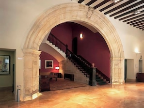 A grand staircase with a marble archway leading to a room with a fireplace, a sofa, and a lamp.