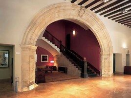 A grand staircase with a marble archway leading to a room with a fireplace, a sofa, and a lamp.