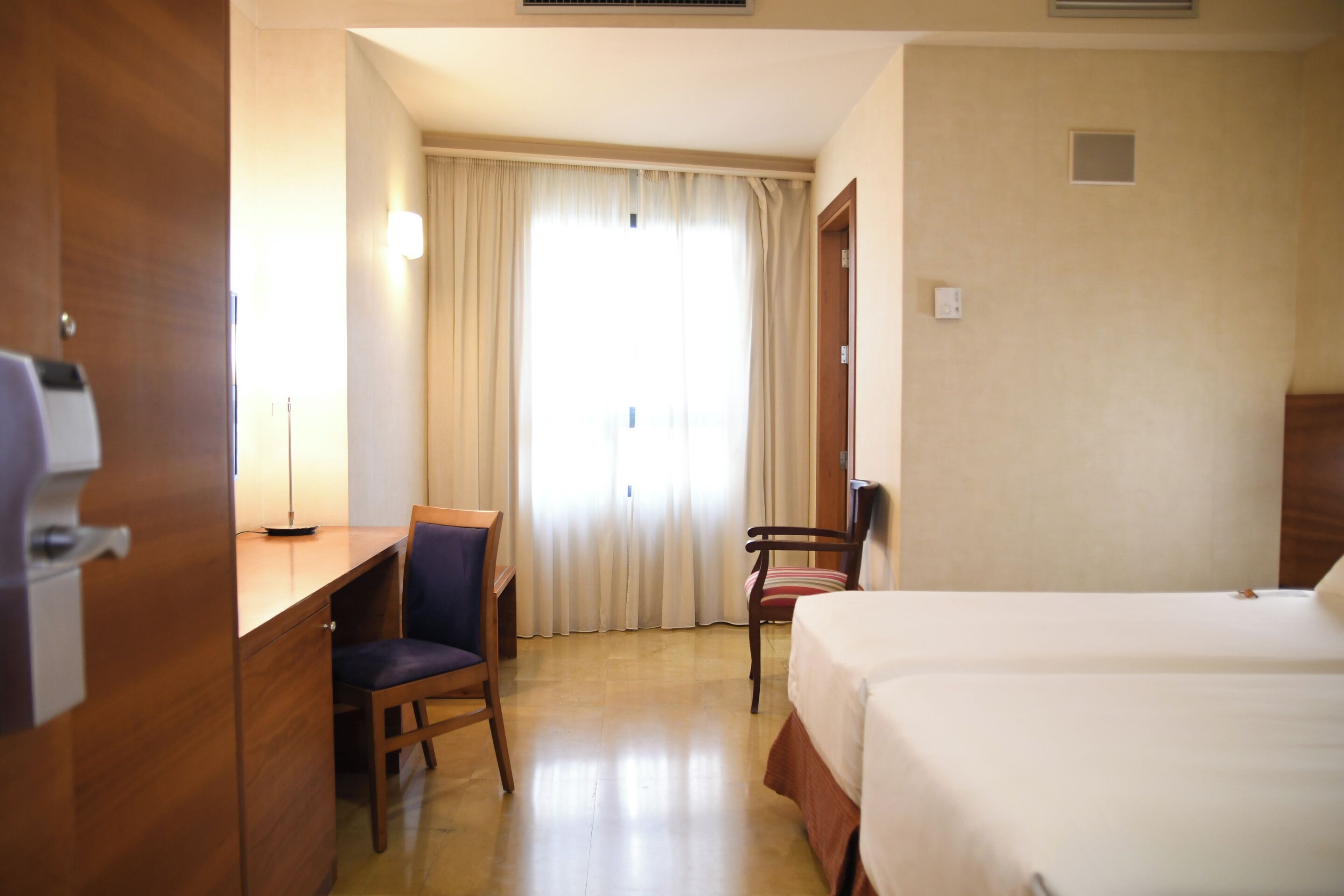 A hotel room with a bed, a desk, a chair, and a window with curtains.