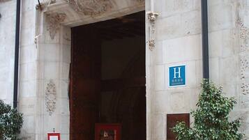 A building entrance with a stone facade, a blue sign with an 'H', and a plaque.