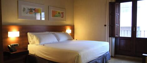 A hotel room with a large bed, bedside lamps, a telephone, and two framed artworks on the wall.