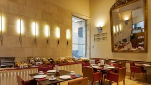 Een eetgedeelte met gedekte tafels voor het ontbijt, een buffet met diverse gerechten, en een grote spiegel aan de muur.