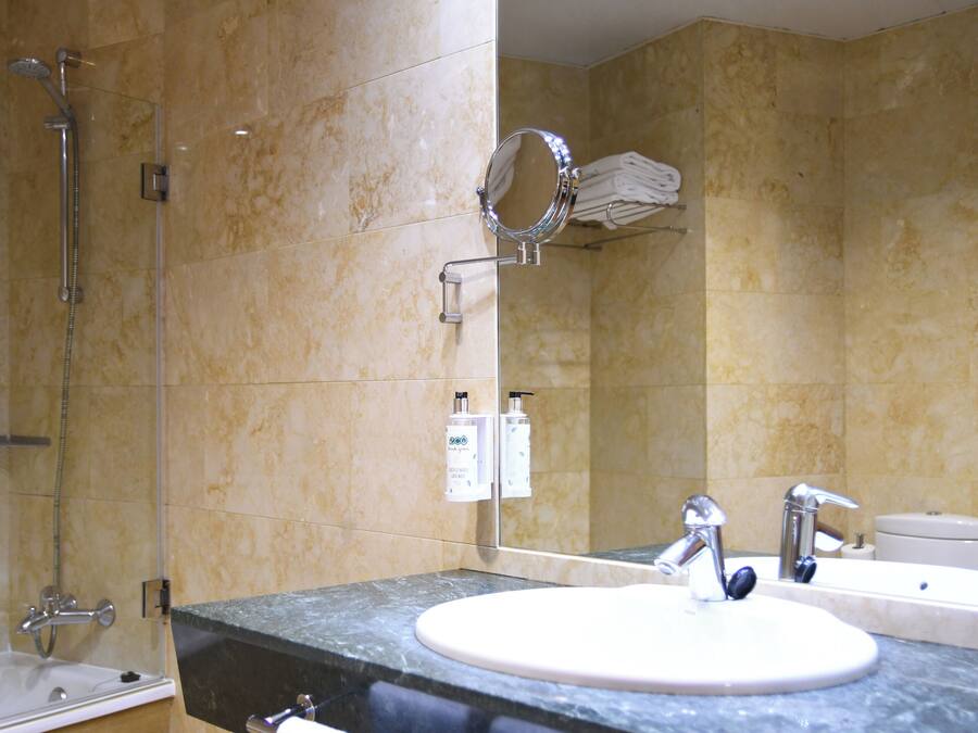 Un baño con bañera, lavamanos, espejo y toallero.