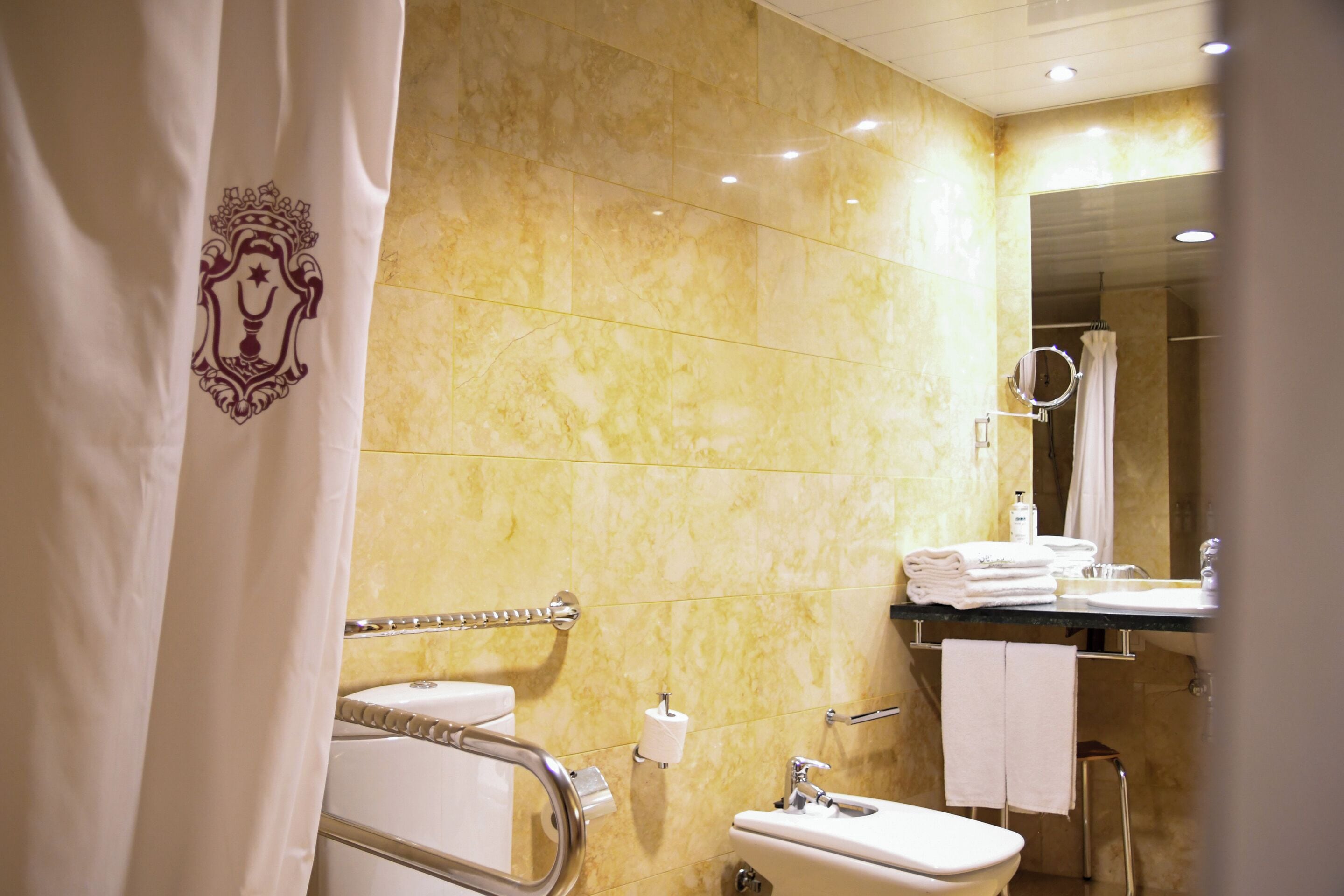 Un bany amb parets de marbre, un lavabo, un vàter i una zona de dutxa.