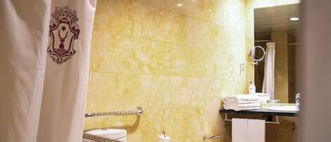 Un bany amb parets de marbre, un lavabo, un vàter i una zona de dutxa.