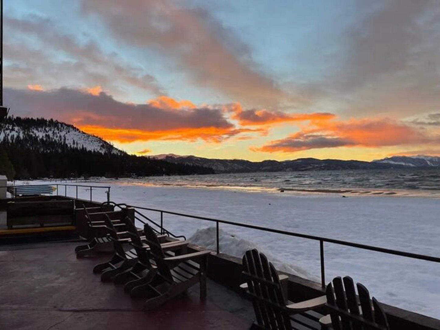 Une terrasse avec des fauteuils Adirondack donnant sur un lac gelé, avec une vue sur le coucher de soleil.
