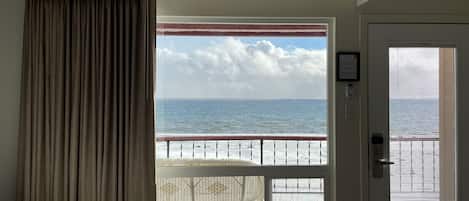 A room with a view of the ocean through a window, a door with a window, and a curtain.