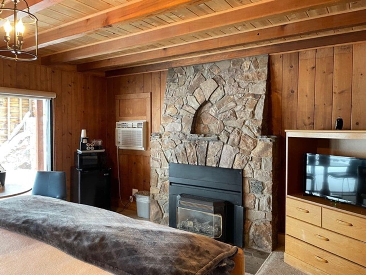 Una habitación acogedora con chimenea de piedra, paredes de madera, televisor y un espacio de descanso confortable.