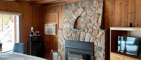 Una habitación acogedora con chimenea de piedra, paredes de madera, televisor y un espacio de descanso confortable.