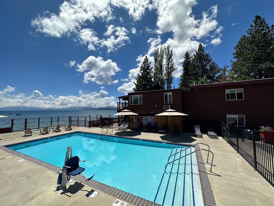 A swimming pool with lounge chairs, a wooden deck, and a view of the ocean and mountains.